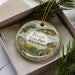 A decorative ornament in a box, featuring a scenic landscape with a lighthouse and greenery, with the text "Perrot State Park, Wisconsin" prominently displayed.
