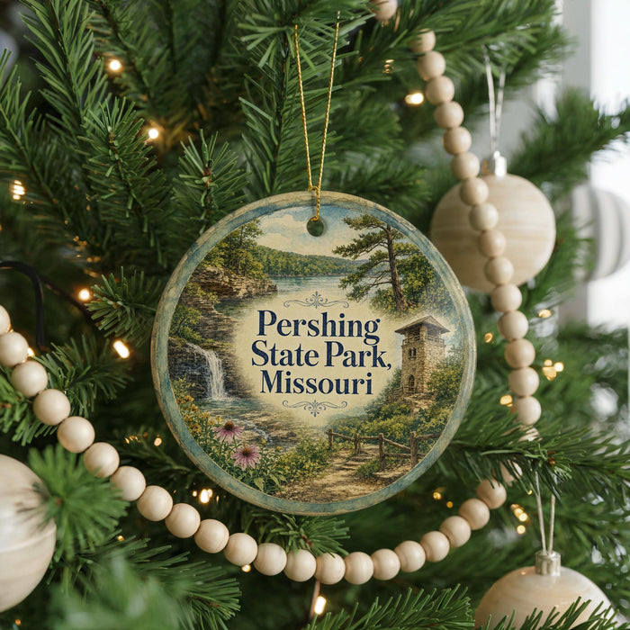 A round ornament hanging on a Christmas tree, featuring a scenic landscape with a waterfall and a castle.