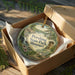 A decorative ornament in a wooden box, featuring a scenic landscape with a waterfall and greenery.