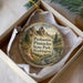A decorative ornament in a box, featuring a scenic landscape with mountains and pine trees.