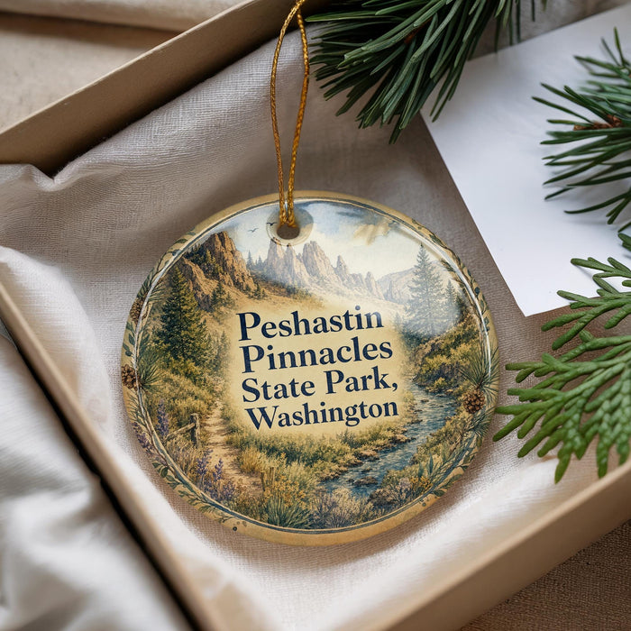 A decorative ornament with a scenic mountain landscape, hanging from a string, placed inside a box with pine branches.