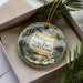 A decorative ornament in a box, featuring a scenic image of Petigrew State Park in North Carolina.