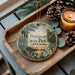A wooden tray with a decorative ornament featuring a scenic landscape of Petigrew State Park, North Carolina, and pine cones.