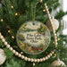A round ornament hanging on a Christmas tree, featuring a scenic landscape with a lake, trees, and a boat.