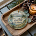 A wooden tray displaying a decorative ornament with a scenic landscape of Placid Lake State Park, Montana, and pine cones.