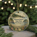 A round ornament with a scenic landscape of a forest, a lighthouse, and a body of water, hanging from a string.