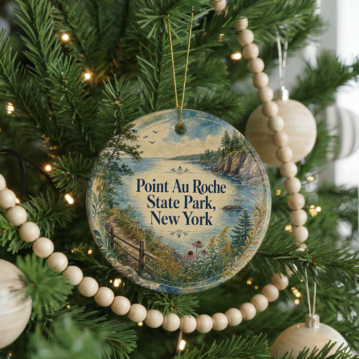 A round ornament hanging on a Christmas tree, featuring a scenic landscape with a body of water and a path leading to a cliff.