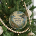 A round ornament hanging on a Christmas tree, featuring a scenic landscape with a body of water and a path leading to a cliff.
