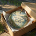 A decorative ornament in a brown box, featuring a scenic landscape with a body of water and trees, with the text "Point Au Roche State Park, New York" printed on it.