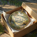 A decorative ornament in a box, featuring a scenic landscape with a waterfall and greenery, with the text "Pomme de Terre State Park, Missouri" printed on it.
