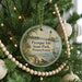 A round ornament hanging on a Christmas tree, featuring a lighthouse and a scenic landscape.
