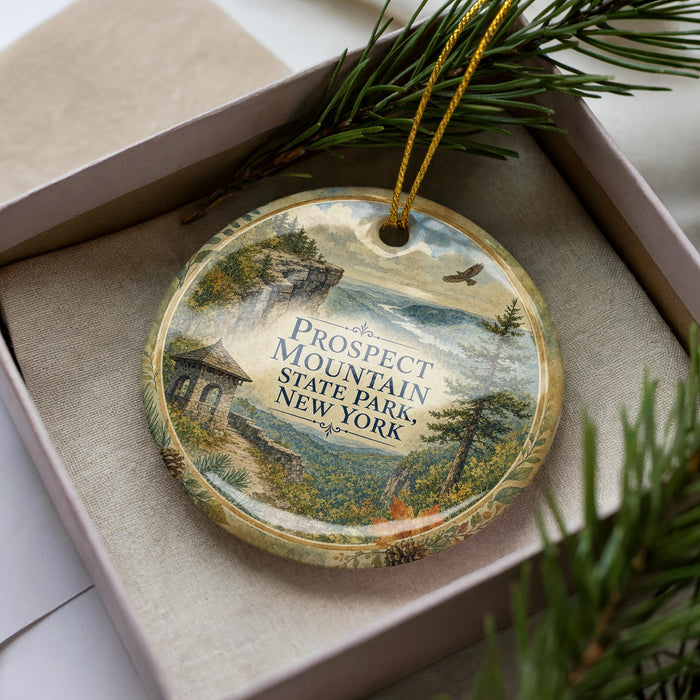 A decorative ornament in a box, featuring a scenic landscape with mountains, trees, and a bird in flight.