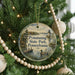 A round ornament hanging on a Christmas tree, featuring a scenic image of a lake and a lighthouse.