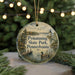 A round ornament with a scenic image of a lake and a lighthouse, surrounded by greenery, hangs in front of a blurred background with twinkling lights.
