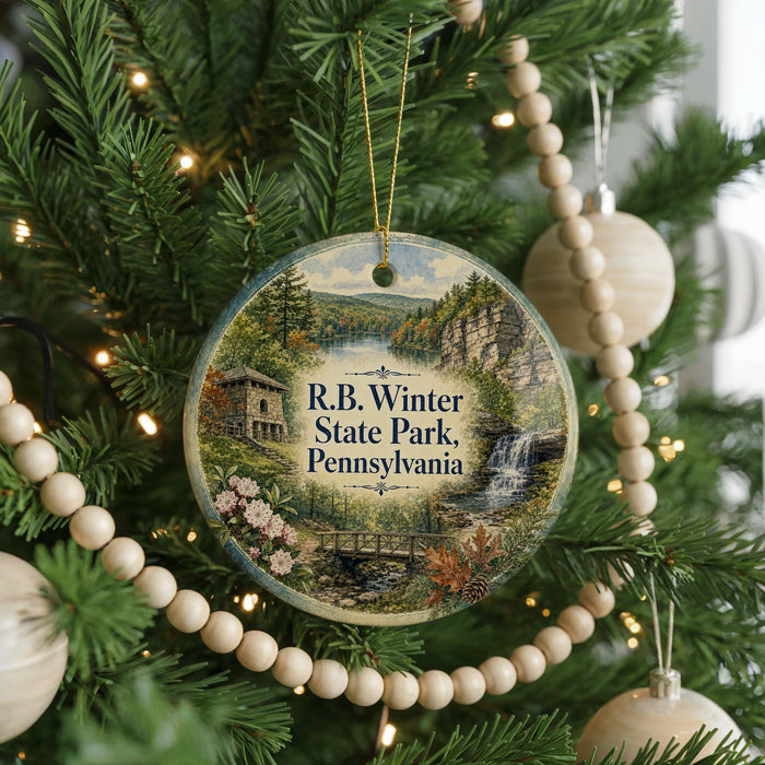 A round ornament hanging on a Christmas tree, featuring a scenic image of Pennsylvania State Park with a waterfall and a bridge.