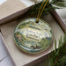A decorative ornament in a box, featuring a bird and a landscape scene with the text "Radnor Lake State Park, Tennessee".
