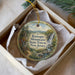 A decorative ornament in a box, featuring a scenic landscape with a waterfall and mountains, along with text that reads "Ramono Mountain State Forest, New Jersey".