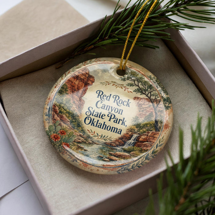 A decorative ornament with a landscape scene featuring a river, mountains, and trees, placed in a box with pine branches.