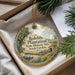 A decorative ornament with a landscape scene and text, placed in a box with pine branches.