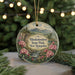 A round ornament with a scenic landscape of mountains, trees, and pink flowers, hanging from a string.