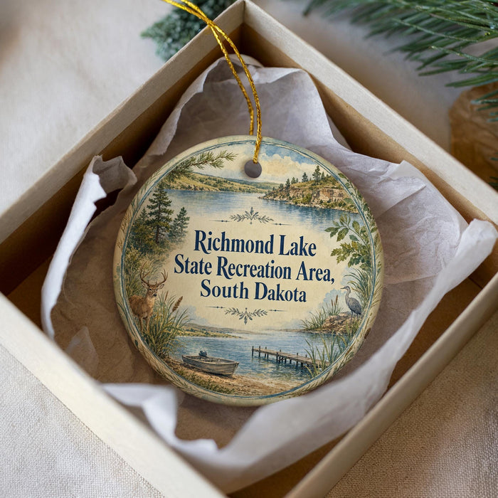 A decorative ornament in a box, featuring a scenic landscape with a lake, trees, and a boat, along with the text "Richmond Lake State Recreation Area, South Dakota".