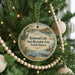A round ornament hanging on a Christmas tree, featuring a scenic image of a lake surrounded by trees and mountains.