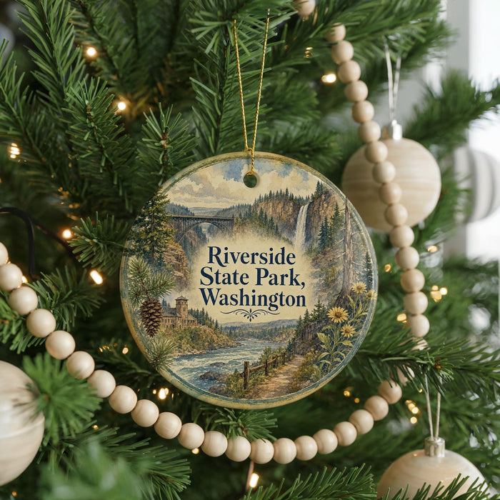 A round ornament hanging on a Christmas tree, featuring a scenic landscape with a waterfall and pine trees.