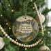 A round ornament hanging on a Christmas tree, featuring a scenic landscape with a waterfall and pine trees.