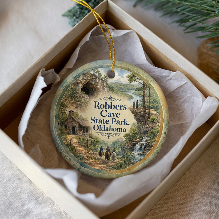 A decorative ornament in a box, featuring a scenic landscape with a cabin, trees, and a waterfall.