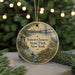 A round ornament with a painting of a park scene, featuring a bridge, a crane, and a person kayaking, hanging from a string.