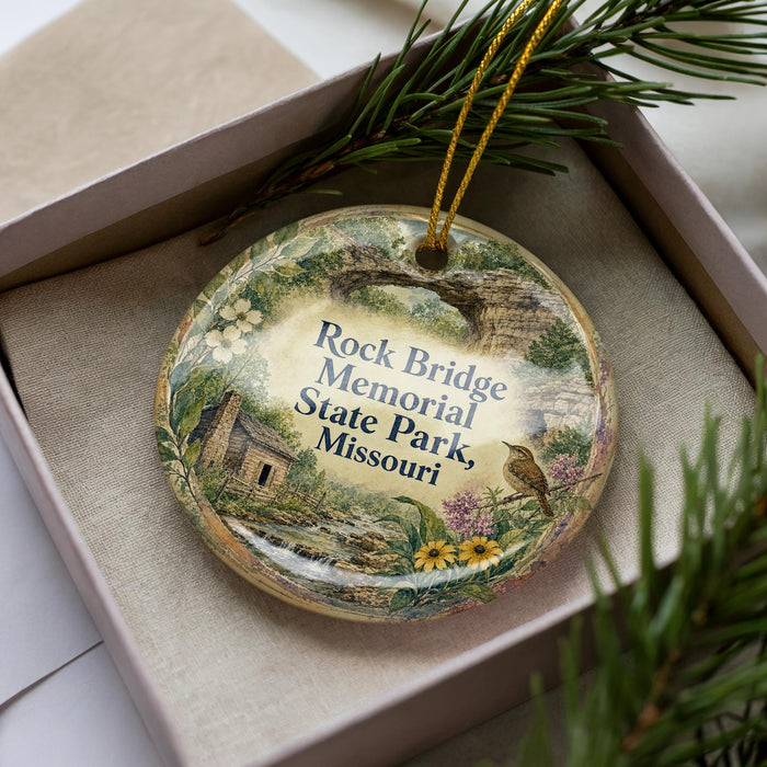 A decorative ornament in a box, featuring a scenic illustration of the Rock Bridge Memorial State Park in Missouri.