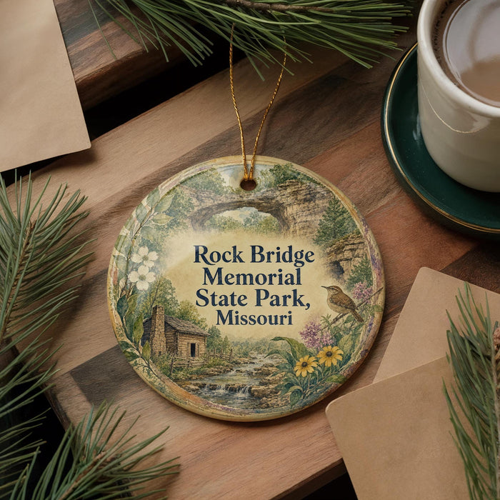 A decorative ornament with a scenic illustration of Rock Bridge Memorial Park, Missouri, featuring a bird perched on a tree branch and a small cabin in the background.
