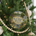 A round ornament hanging on a Christmas tree, featuring a scenic landscape with a waterfall and a house.