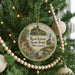A round ornament hanging on a Christmas tree, featuring a scenic landscape with a lighthouse and a bird.
