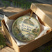 A decorative ornament in a wooden box, featuring a scenic landscape with a lighthouse and a small island, with the text "Rock Island State Park, Wisconsin" printed on it.