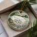A decorative ornament in a box, featuring a scenic landscape with a lake, trees, and a bird, along with the text "Rockland Lake State Park, New York".