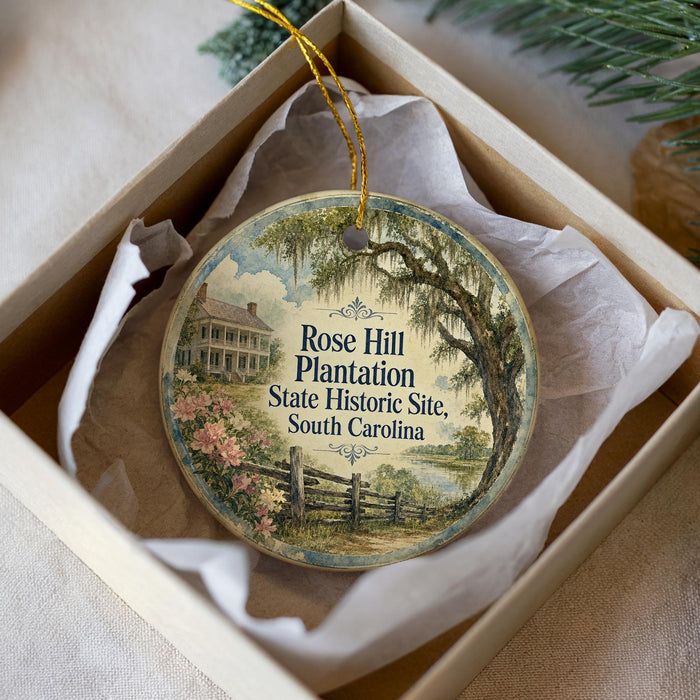 A round ornament with a vintage-style illustration of a house and a tree, placed in a white box with a gold string.