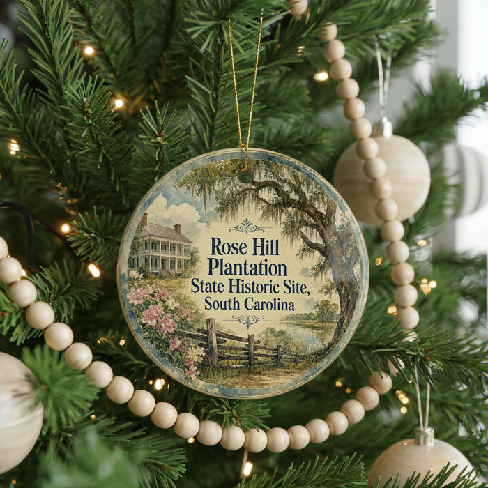 A round ornament hanging on a Christmas tree, featuring a scenic image of a house surrounded by trees and a pond.