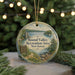 A round ornament with a scenic landscape of a lake, mountains, and a building, surrounded by greenery and a string of lights.