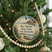 A round ornament hanging on a Christmas tree, featuring a lighthouse and a boat on the water.