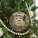 A round ornament hanging on a Christmas tree, featuring a scenic landscape with mountains, a lake, and a bird.