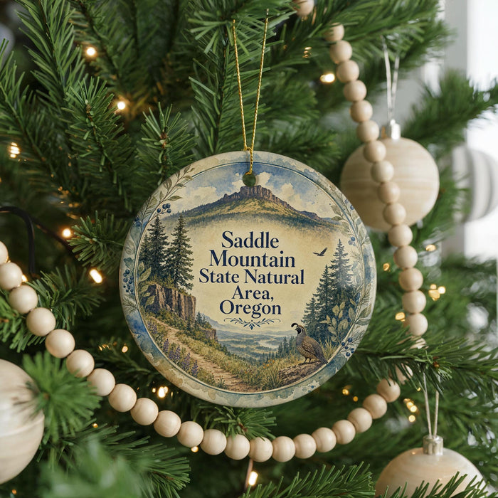 A round ornament hanging on a Christmas tree, featuring a scenic landscape with mountains, trees, and a bird.