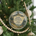 A round ornament hanging on a Christmas tree, featuring a scenic landscape with mountains, trees, and a bird.