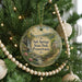 A round ornament hanging on a Christmas tree, featuring a scenic landscape with a waterfall and a house.