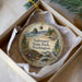 A decorative ornament in a white box, featuring a scenic landscape with a body of water, trees, and a bird.