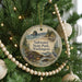 A round ornament hanging on a Christmas tree, featuring a scenic landscape with a beach, mountains, and a bird.