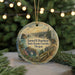 A round ornament with a scenic landscape depicting a mountain range, river, and forest, hanging from a string.