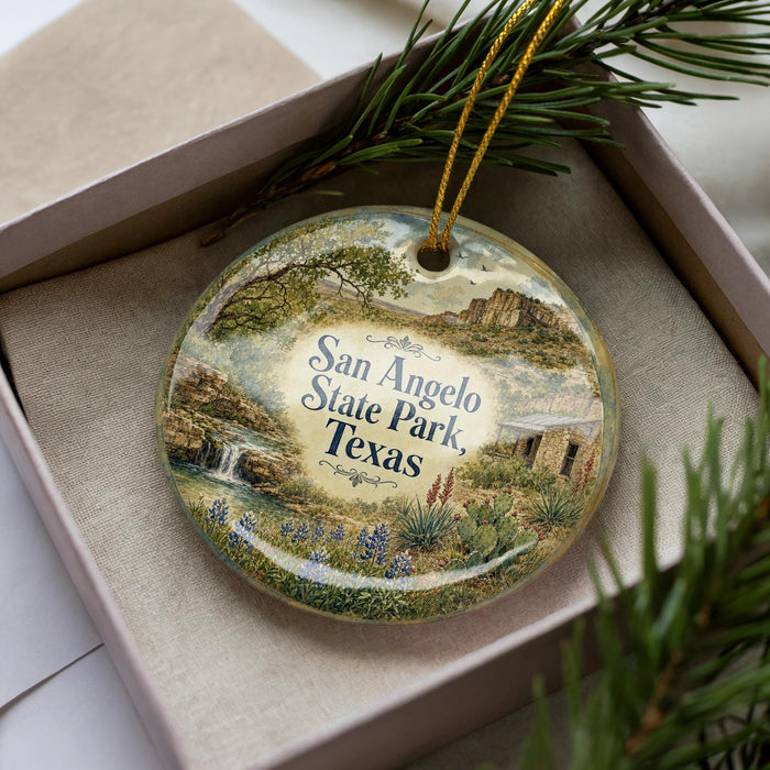 A decorative ornament in a box, featuring a scenic landscape with mountains, waterfalls, and wildflowers.