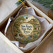 A decorative ornament in a box, featuring a scenic landscape with a waterfall, desert, and a small building.