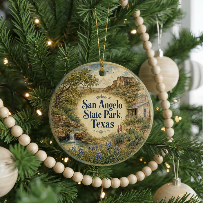 A round ornament hanging on a Christmas tree, featuring a scenic landscape of San Angelo State Park, Texas.